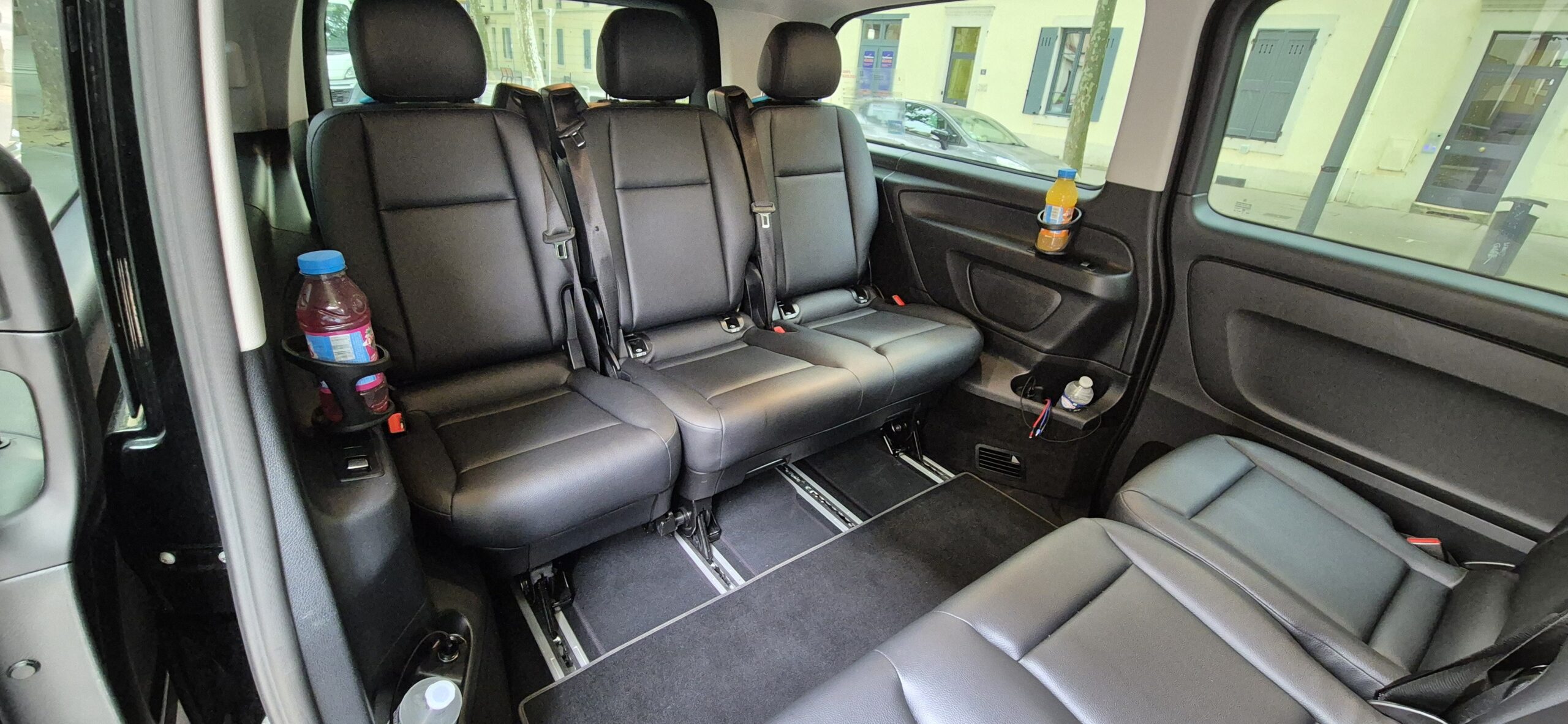 Intérieur spacieux d'un taxi Mercedes Vito pouvant accueillir jusqu'à 8 passagers avec sièges en cuir noir et boissons fraîches.
